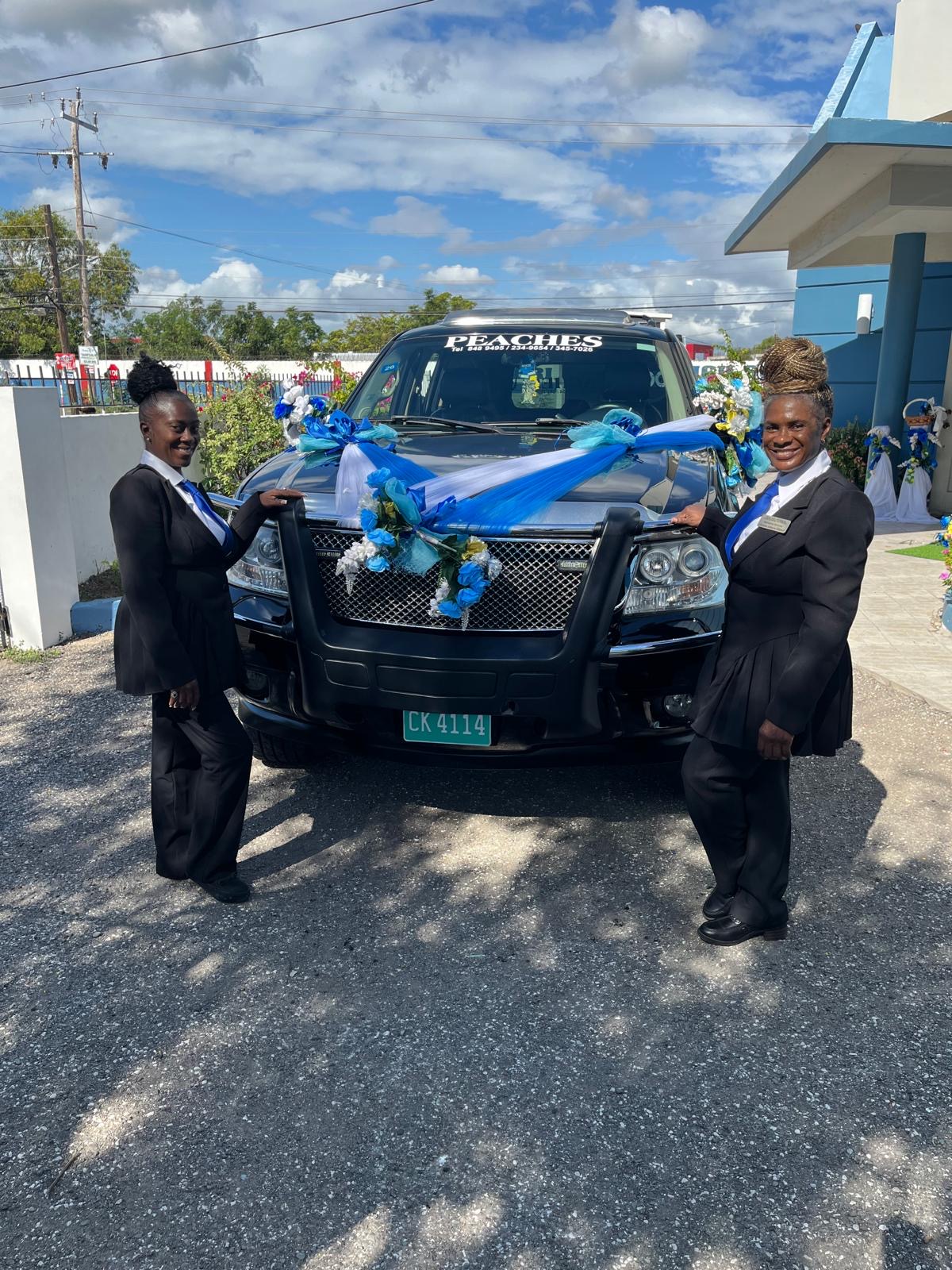 Two members of the Peaches team beside the black SUV dressed in blue and white drapes and flowers